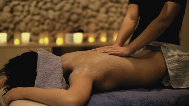 A Person Lying Face Down on A Massage Table, Receiving a Soothing Back Massage in A Dimly Lit, Candle-Lit Spa Room, Creating a Calming Ambiance